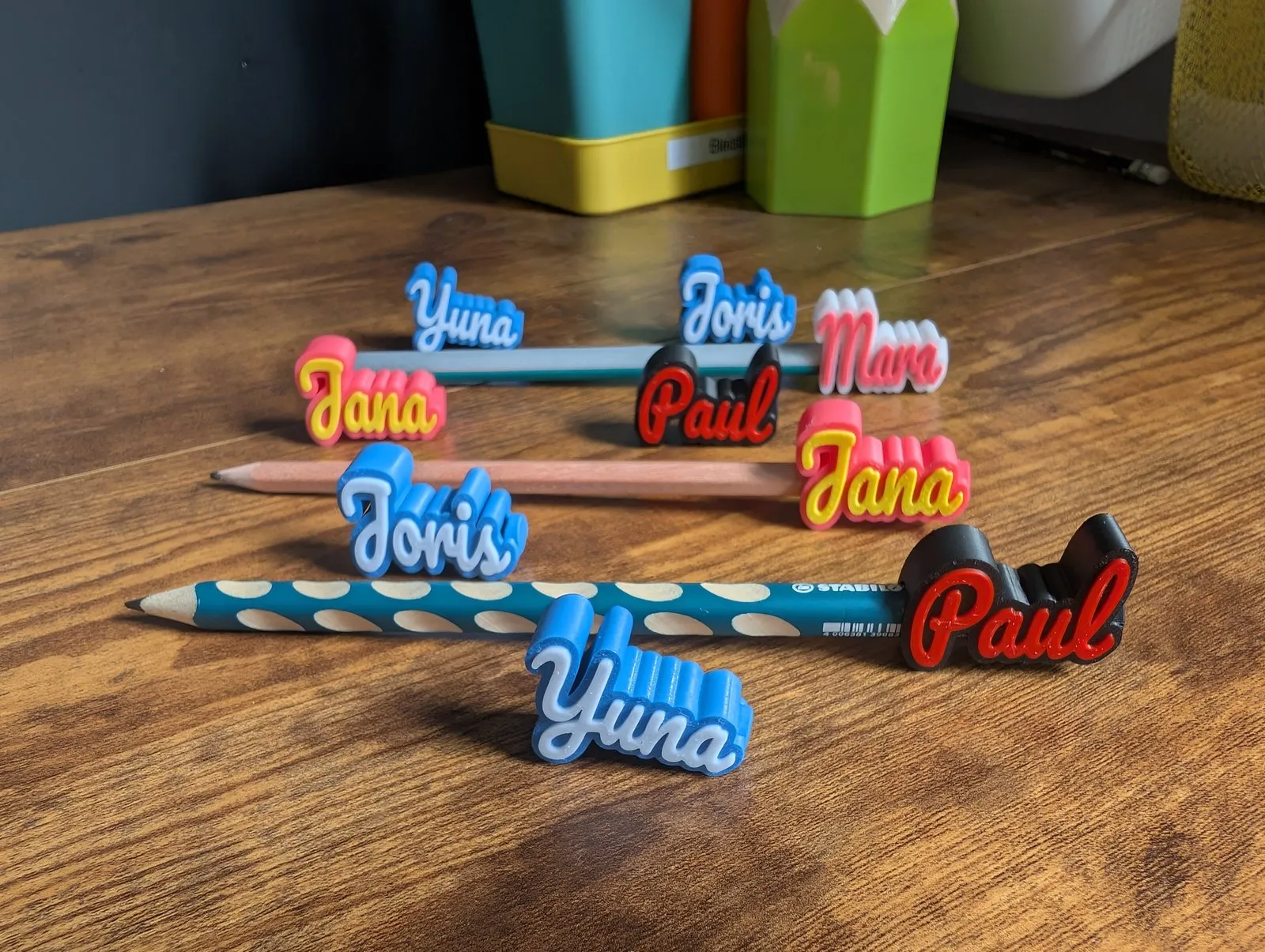Personalisierte Stiftaufsätze mit den Namen 'Paul', 'Yuna' und 'Mara' auf Buntstiften